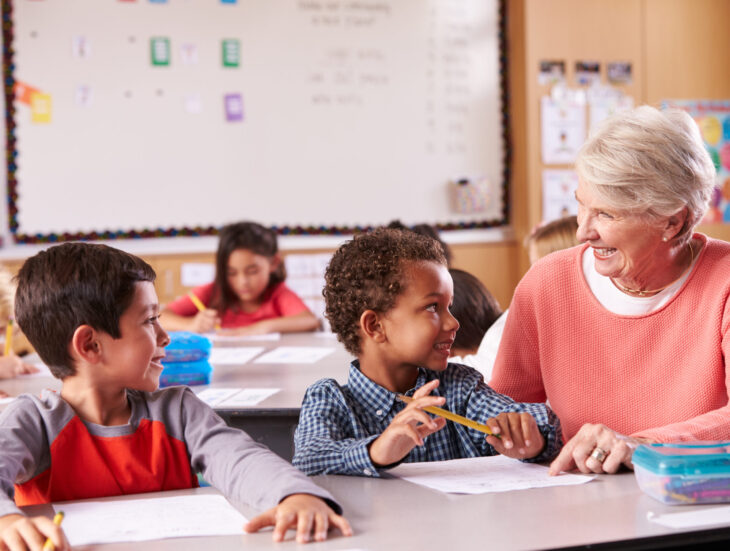 Senior teacher sitting with elementary school kids in class