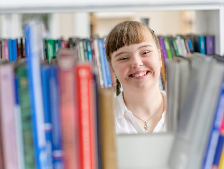 Girl with syndrome down chooses a book on a shelf in the library