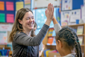 A happy elementary school teacher gives a high five to a smiling student during class.